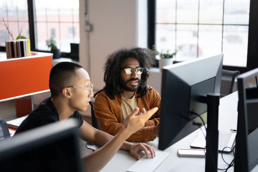 Two men with glasses looking at a monitor in an office and pointing at the monitor